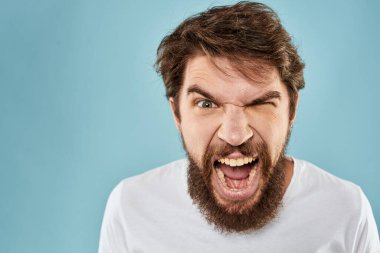 Sakallı adam duyguları, yüz ifadesi el hareketleriyle mavi arka planı kapatır.