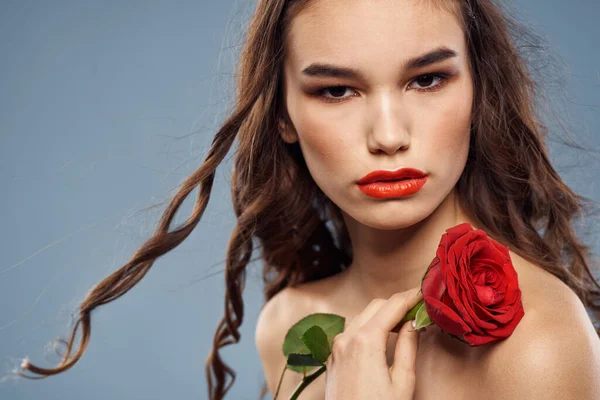 Žena portrét s červenou růží v blízkosti obličeje na šedém pozadí a make-up kudrnaté vlasy — Stock fotografie