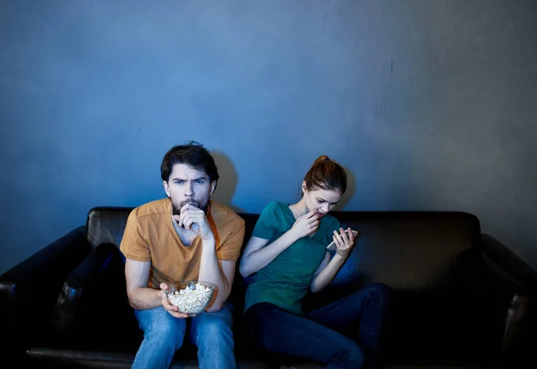 Un hombre emocional y una mujer bonita en el sofá están viendo la televisión con interés en una habitación oscura — Foto de Stock