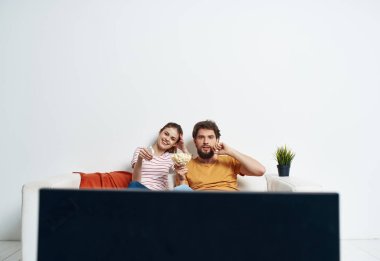 Erkek ve kadın kanepede, çiçek odasının içi ve televizyon ekranlı.