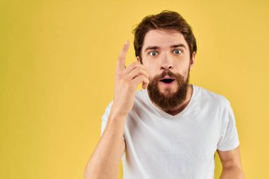 Sakallı adam duyguları, elleri beyaz tişörtlü, sarı arka planlı eğlenceli bir jest.