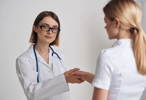 Vrouw arts in een medisch toga schudt handen met een patiënt in een wit t-shirt op een lichte achtergrond — Stockfoto