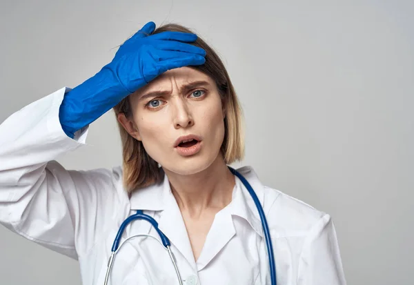 Una enfermera con un vestido médico y guantes azules gestos con un estetoscopio alrededor de su cuello —  Fotos de Stock