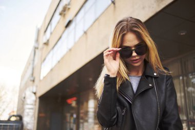 Güneş gözlüklü, sarışın, deri ceketli şık bir kadın.