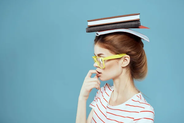 Étudiante avec des livres sur la tête et des lunettes jaunes sur fond bleu vue recadrée — Photo