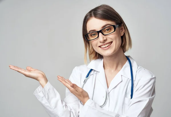 Kvinnlig sjuksköterska i medicinsk klänning gestikulerande med händerna på ljus bakgrund beskärd vy — Stockfoto