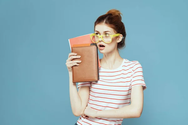 Женщина-студентка с книгами в руках на синем фоне и в желтых очках модель прически обрезанный вид — стоковое фото