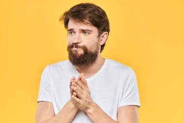 Sakallı adam duyguları, yüz ifadesi, beyaz tişört, sarı arka plan.