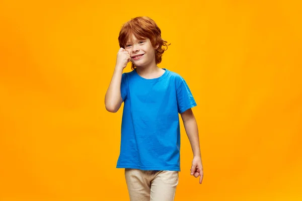 Χαρούμενα κόκκινα μαλλιά αγόρι χαμόγελο χέρι στο πρόσωπο μπλε t-shirt τζιν κίτρινο φόντο — Φωτογραφία Αρχείου