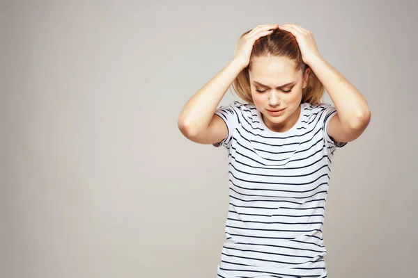 Eine Frau im gestreiften T-Shirt hält ihre Hände vor ihrem emotionalen Unbehagen hellen Hintergrund — Stockfoto