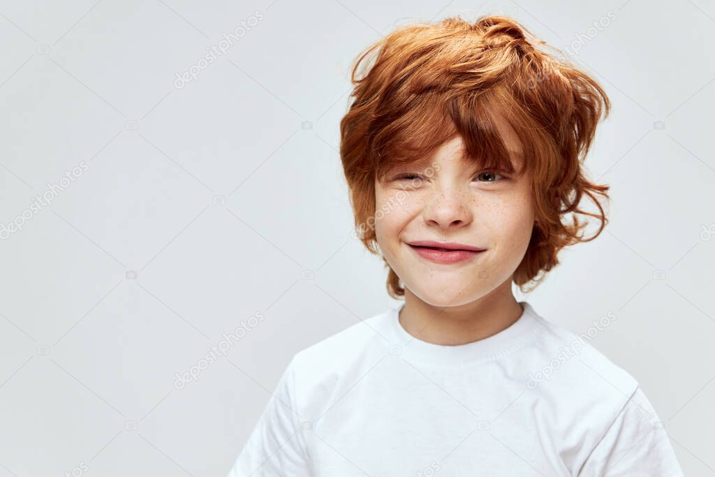 Sly red-haired boy with narrowed eyes conceived something bad white t-shirt cropped view 