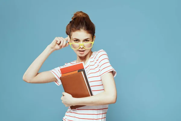 Étudiante avec des livres dans les mains sur un fond bleu et modèle de lunettes jaunes coiffure vue recadrée — Photo