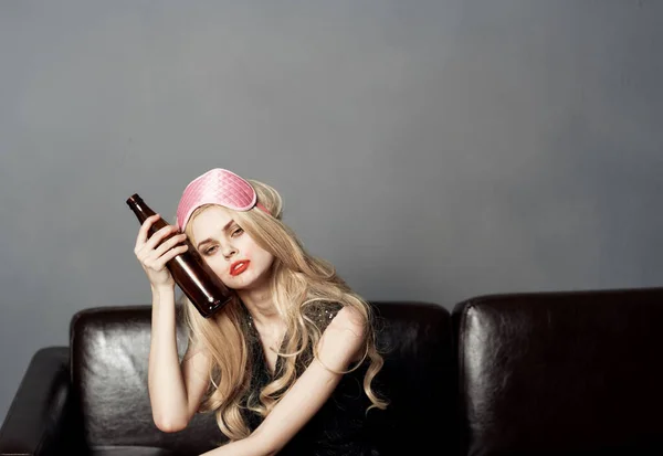 Woman with bottle of beer on sofa alcohol addiction sleep mask on head — Stock Photo, Image