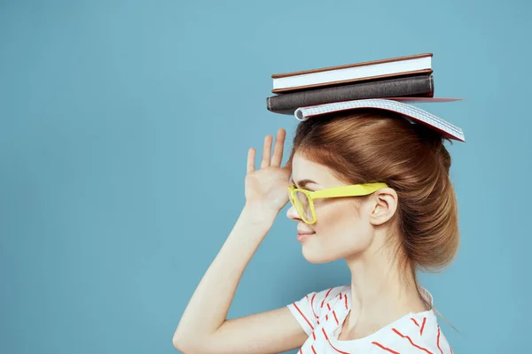 Vrouwelijke studente met boeken op haar hoofd en in gele bril op een blauwe achtergrond bijgesneden uitzicht — Stockfoto