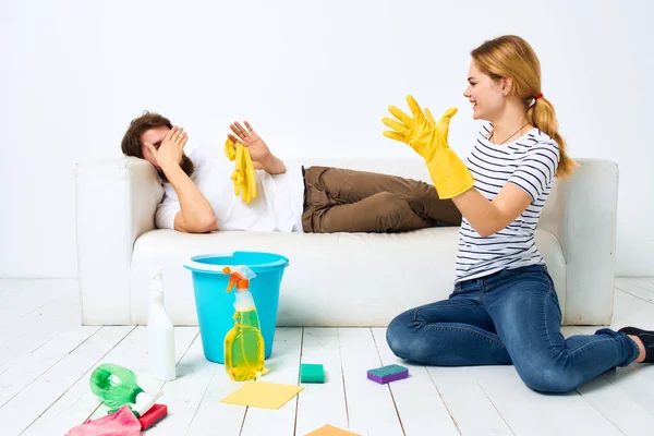 The wife cleans up while the husband lies on the couch interior housework — Stock Photo, Image