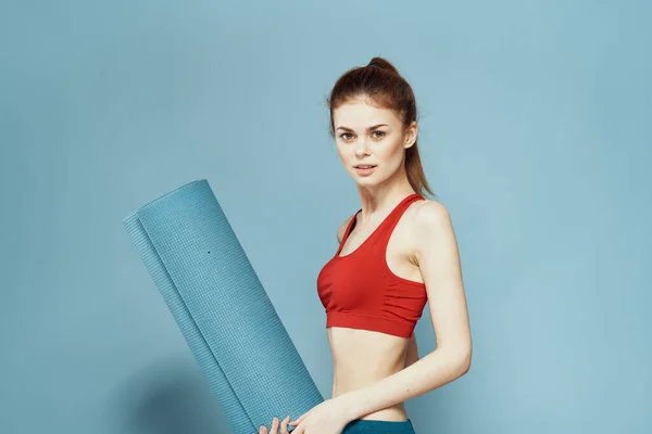Donna atletica con fitness mat esercizio fisico sottile figura rossa t-shirt sfondo blu — Foto Stock