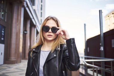 Deri ceketli mutlu kadın manken sokakta yürüyor.