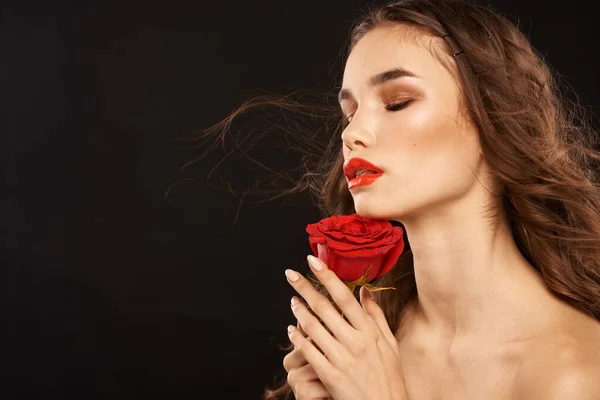 Žena s červenou růží na tmavém pozadí dlouhé vlasy make-up červené rty — Stock fotografie