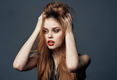 Kırmızı dudaklı ve gri arka planda siyah elbiseli bir kadın elleriyle yüzüne dokunuyor.