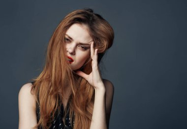 Kırmızı dudaklı ve gri arka planda siyah elbiseli bir kadın elleriyle yüzüne dokunuyor.