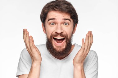 Beyaz tişörtlü neşeli sakallı adam elleri arka plandaki stüdyoyu aydınlatıyor.