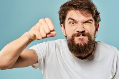 Sakallı adam duyguları, yüz ifadesi el hareketleriyle mavi arka planı kapatır.