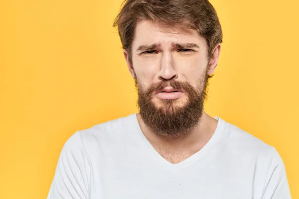 하얀 티셔츠를 입고 노란 배경을 가진 남자의 얼굴 표정을 하고 있는 수염 남자의 감정 — 스톡 사진