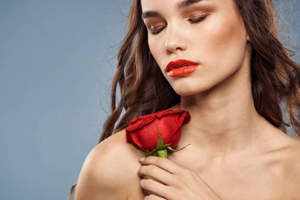 Γυναίκα πορτρέτο με κόκκινο τριαντάφυλλο κοντά στο πρόσωπο σε γκρι φόντο και μακιγιάζ σγουρά μαλλιά — Φωτογραφία Αρχείου