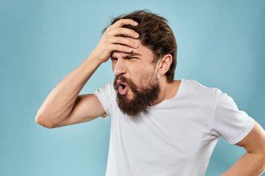 Huysuz yüz ifadesi olan bir adam. Stüdyo tarzı mavi arka planda el kol hareketi yapıyor.