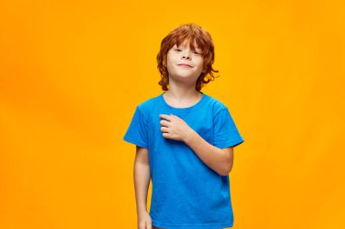 Mavi tişörtlü kızıl saçlı çocuk. Önden sarı arka plan. 