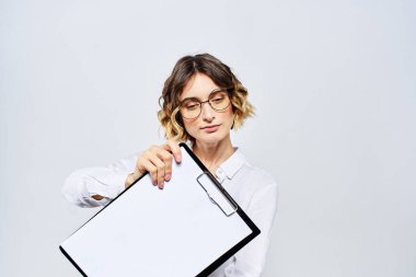 Elinde beyaz dökümanların olduğu bir klasör olan iş kadını arka planda ve saç stili gözlüklü model