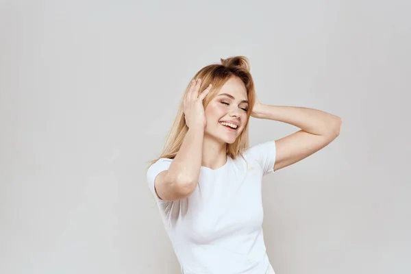 Loira alegre em uma camiseta branca gesticulando com as mãos luz de fundo — Fotografia de Stock