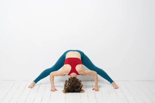 Sports woman in a bright room doing yoga in full growth blue leggings and a red tank top — Stock Photo, Image