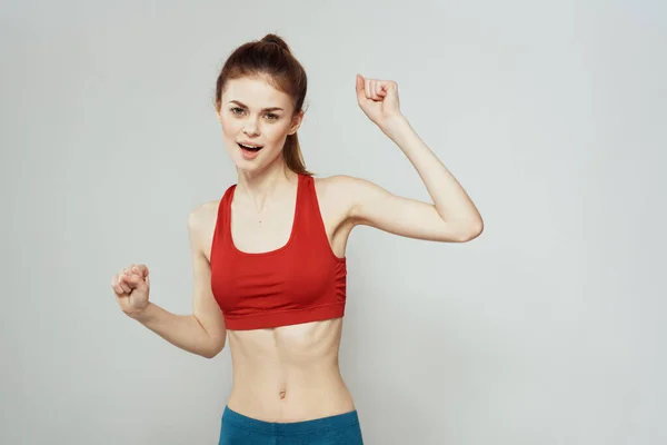 Een vrouw in een rood T-shirt op een lichte achtergrond is bezig met fitness gebaren met haar handen een slank figuur — Stockfoto