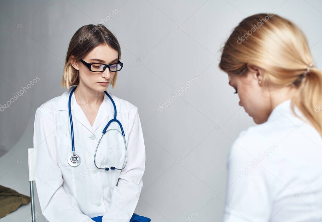 Doctor sits on a chair and a woman patient indoors on a light background
