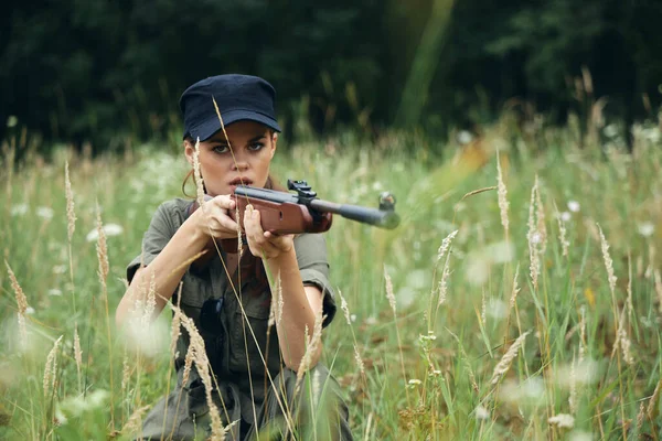 Mulher militar Abrigo senta-se na grama arma de caça folhas verdes — Fotografia de Stock