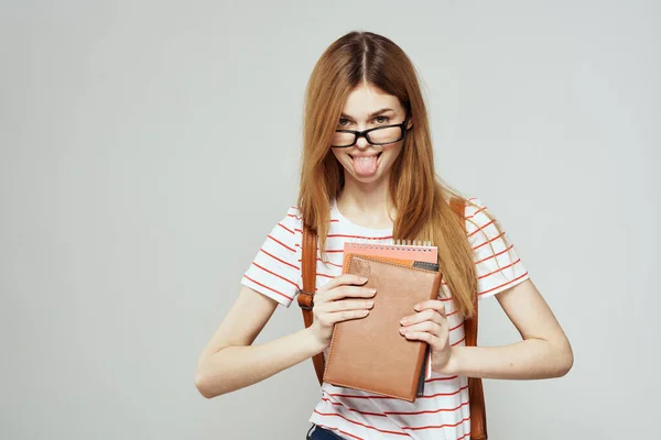 Estudante feminina com bloco de notas e óculos em um fundo leve vista cortada de uma camiseta listrada — Fotografia de Stock