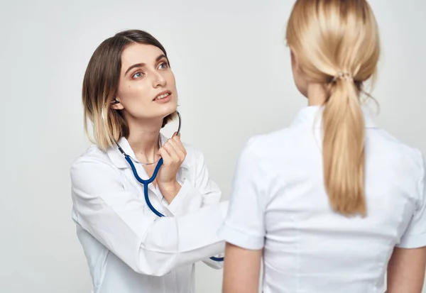 En sjuksköterska i medicinsk klänning förklarar något för en patient i en vit t-shirt — Stockfoto