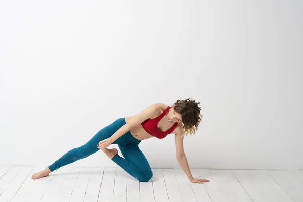 Een vrouw in blauwe jeans oefent yoga op een lichte achtergrond binnen en een slanke figuur in gymnastiek — Stockfoto