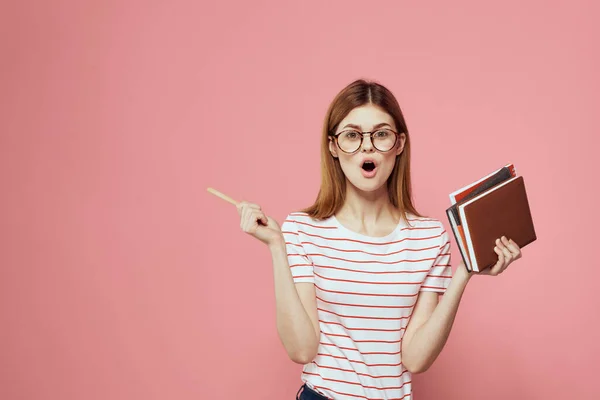 Vrouwelijke student met notitieblokken op roze achtergrond gebaren met haar handen bril op haar gezicht gestreepte t-shirt model — Stockfoto