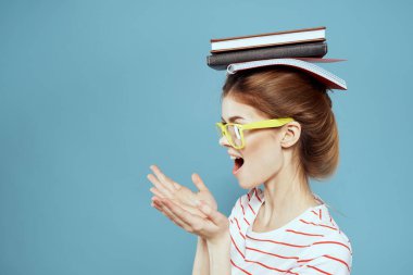 Kafasında kitaplarla, mavi arka planda sarı gözlüklü bir bayan öğrenci.
