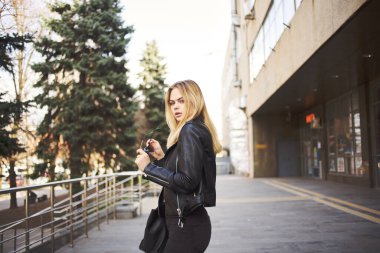 Deri ceketli bir kadın binanın yanında yürüyor.