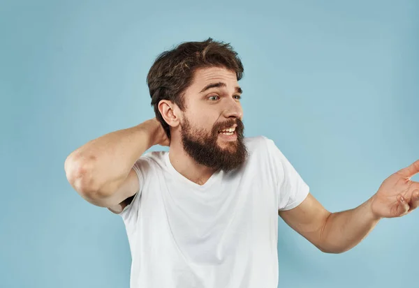 Веселий хлопець у футболці з бородою на синьому фоні тримає руку за голову — стокове фото