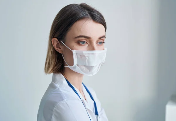 Mulher enfermeira em máscara médica azul estetoscópio luz fundo — Fotografia de Stock