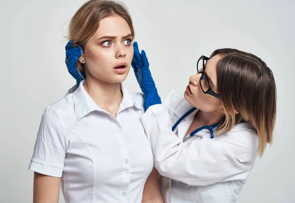 Un medico donna in abito medico e guanti blu esamina il volto dei pazienti — Foto Stock
