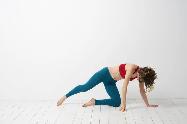 Een vrouw in blauwe jeans oefent yoga op een lichte achtergrond binnen en een slanke figuur in gymnastiek — Stockfoto