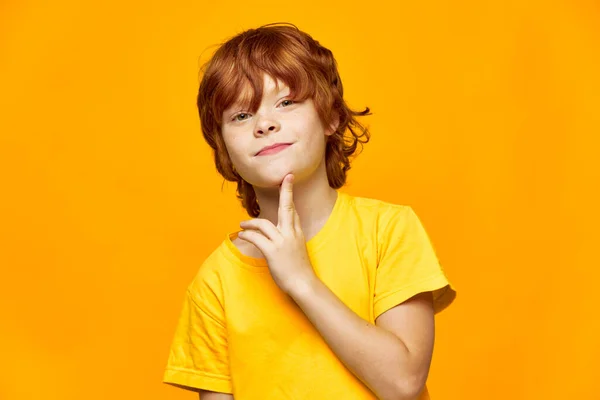 Uśmiechnięte rudowłose dziecko na żółtym tle trzyma rękę blisko twarzy, — Zdjęcie stockowe