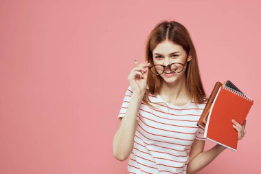 Elinde kitap tutan güzel bir kız öğrenci. El hareketleriyle el hareketi yapıyor. Pembe arka plan.