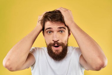 Beyaz tişörtlü bir adam, el hareketleriyle sarı arka plan manzarasını daha eğlenceli kılıyor.