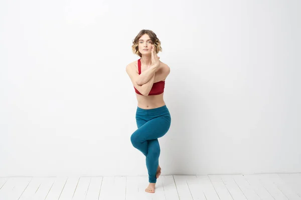 Mujer deportiva en una habitación luminosa haciendo yoga en leggins azules de pleno crecimiento y una camiseta roja — Foto de Stock